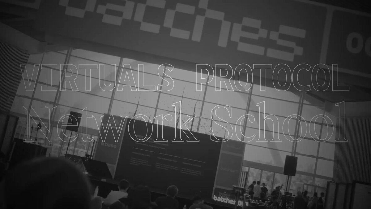 The image shows a large screen displaying the words "Virtuals Protocol and Network School" written in white text against a black background. The screen also features an image of people gathered around a stage with microphones, suggesting that there might be a live event or presentation taking place at this school.