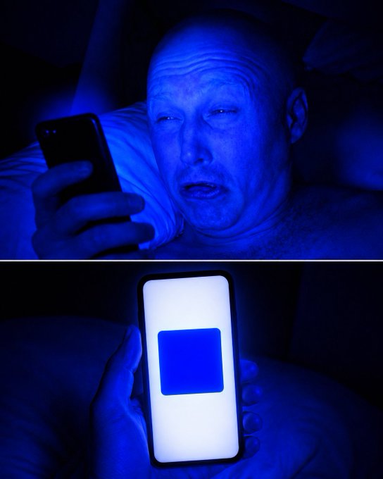 A man lies in bed bathed in blue light, his face illuminated by the glow of a smartphone he's holding, with the screen displaying a bright blue square logo—the Base (BASE) cryptocurrency logo. The image humorously captures the post's sentiment of waking up "bullish on @base," with the blue glow and wide-eyed expression suggesting an intense, almost startled enthusiasm for the crypto project.