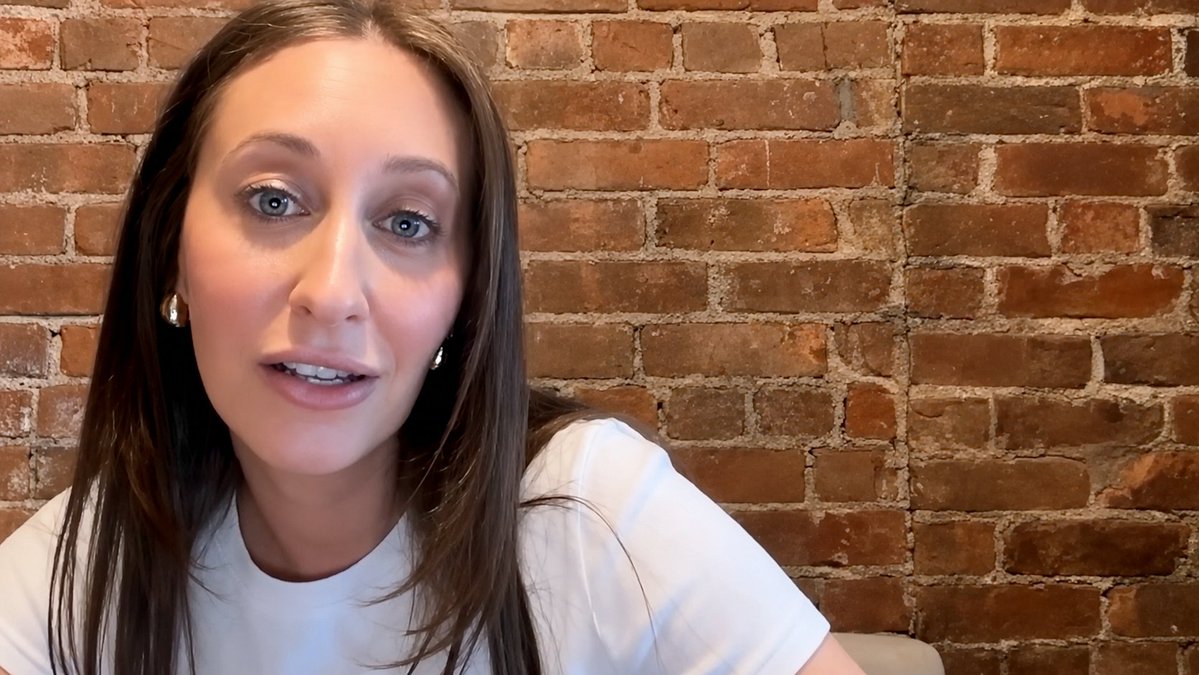 A woman with long brown hair and blue eyes speaks to the camera against a brick wall, delivering commentary on why Avalanche technology stands out as a top choice for business applications.