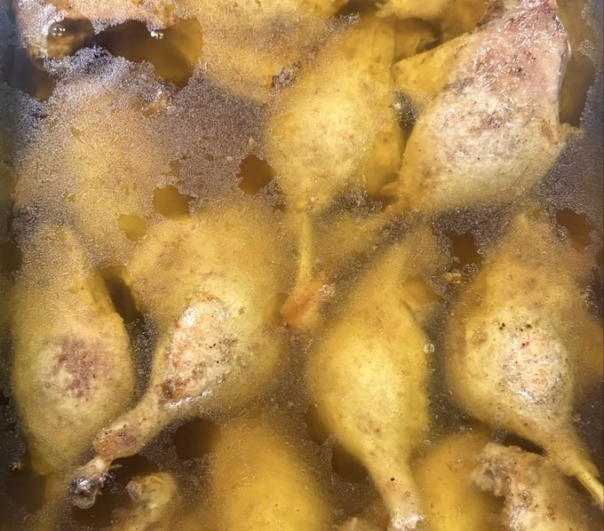Frozen chicken drumsticks packed together in a bag, coated with a yellow seasoning.