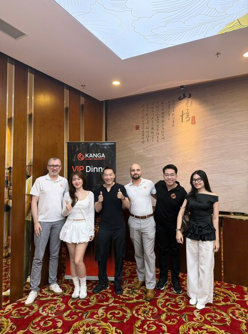 Six people pose together for a group photo in front of a 'KANGA' VIP Dinner banner in a decorated indoor venue.