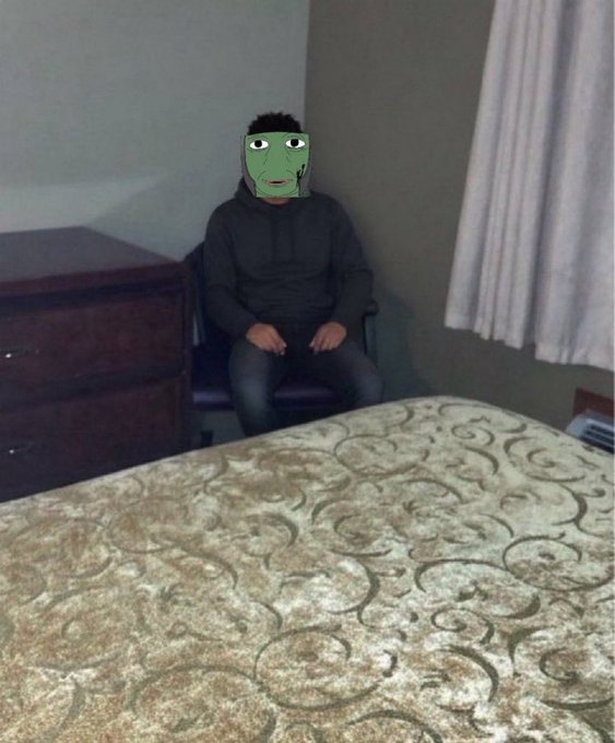 A person sits in a chair in a dimly lit room, their face humorously obscured by a Pepe the Frog meme, fitting the post's joke about grown men disguising themselves while purchasing Ansem the black bull.