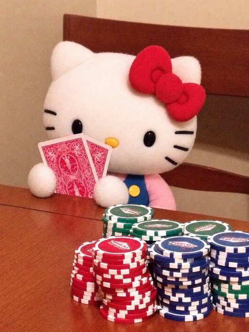 A Hello Kitty plushie holds two red playing cards behind stacks of red, green, and blue casino poker chips on a wooden table. The cute, lighthearted scene plays on the "$kitty" theme, with Hello Kitty herself personifying the pun in a casino-style gambling setting.