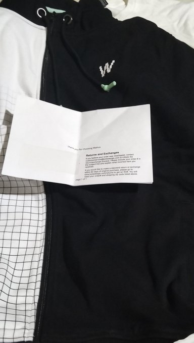 A black hoodie with a white 'W' logo lies flat with an open instruction booklet on top, showing a page titled 'Returns and Exchanges'.