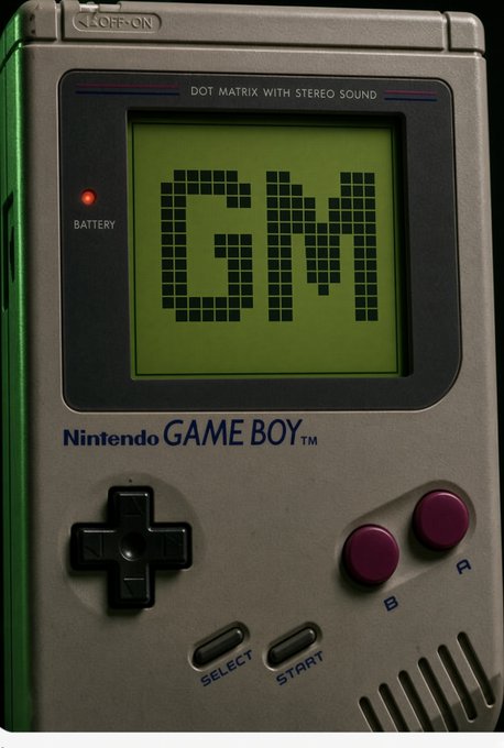 A close-up, detailed rendering or photograph of the classic original Nintendo Game Boy, showing its green screen displaying "GM" in dot matrix text, with the directional pad, A/B buttons, and Select/Start buttons visible.
