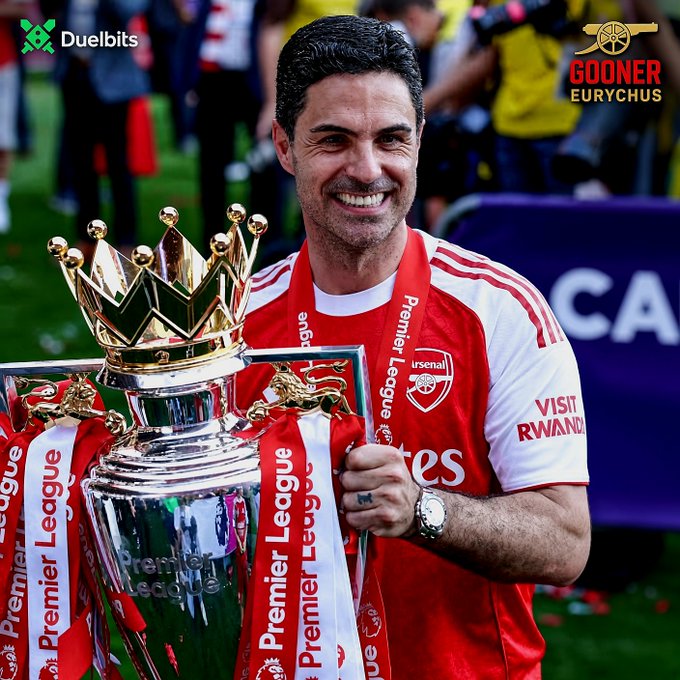 Mikel Arteta, manager of Arsenal, proudly holds the Premier League trophy adorned with red and white ribbons while wearing the club's jersey featuring the "Visit Rwanda" and "Emirates" sponsorships. The image, watermarked with "Duelbits" and "Gooner Eurychus," visually reinforces the post's message of triumphant resilience—comparing Arsenal's successful rise under Arteta to Duelbits' comeback after being "hacked."