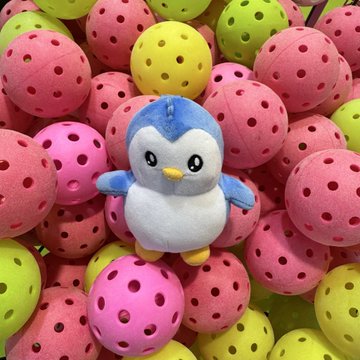 A small plush penguin toy resting in a pit filled with colorful wiffle balls in pink, yellow, and green.