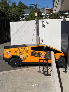 An orange and black KFC-branded Lamborghini-style vehicle with a cat character graphic parked on a street next to a small table.