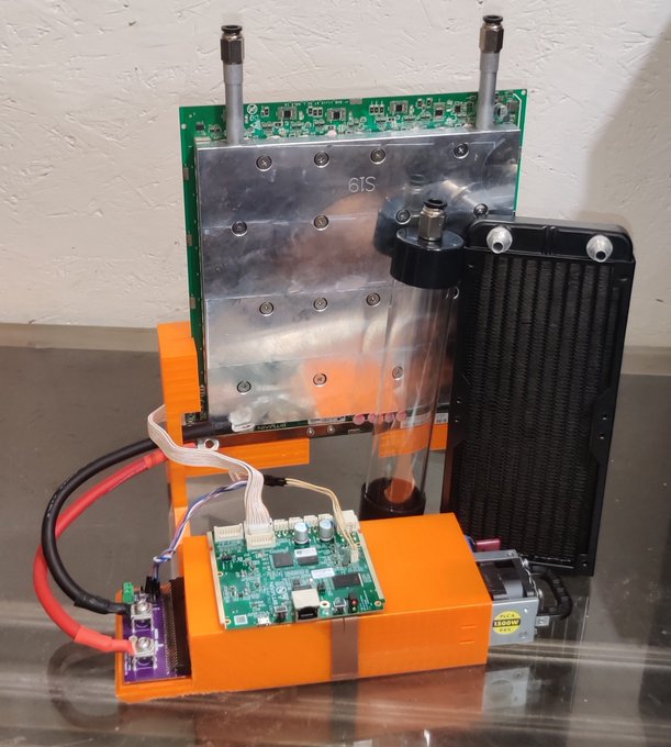 An orange electronic device assembly featuring circuit boards, a radiator, and what appears to be a '6TS' labeled component mounted on a metal plate.