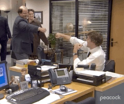 The image shows a man sitting at his desk, wearing glasses and holding a cell phone up to his face as if taking a picture or recording something. The scene takes place in an office setting with several people present, including two men standing near the window and another person seated at their desk. There are also various objects on the desks such as a keyboard, mouse, potted plant, and books. A computer monitor is visible in the background, suggesting that this gathering might be taking place during work hours or possibly an office party. The post about the museum seems to be unrelated to the scene depicted in the image, but it could be a reference to the man's job at the museum or his interest in museums.