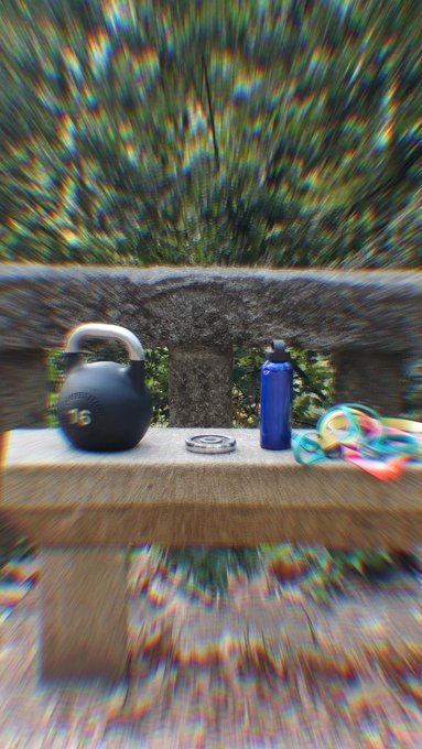 An outdoor bench scene with a black kettlebell, blue water bottle, and colorful resistance bands, treated with a heavy distortion or glitch filter effect.