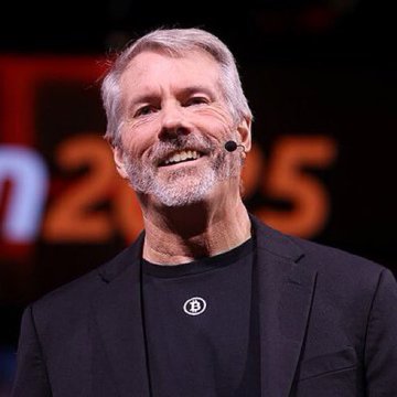 Michael Saylor smiles while speaking on stage, with "2025" visible in the blurred background. The image relates to the news of his company, Strategy, selling 1,690 bitcoin for $108.6 million at an average price of $64,262.
