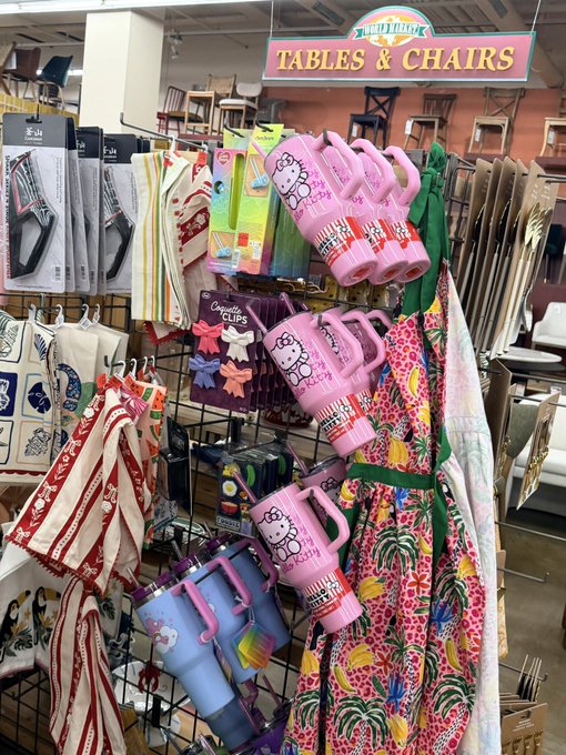 A retail store display under a 'TABLES & CHAIRS' sign features colorful merchandise including Hello Kitty thermoses/tumblers, patterned aprons, kitchen towels, and gardening tools.