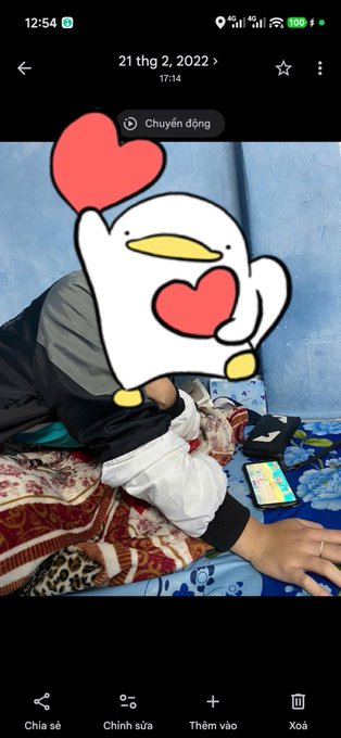 A smartphone screenshot from a photo gallery showing a person lying on a bed with a large cartoon duck sticker covering their face, displaying the date 21 thg 2, 2022.