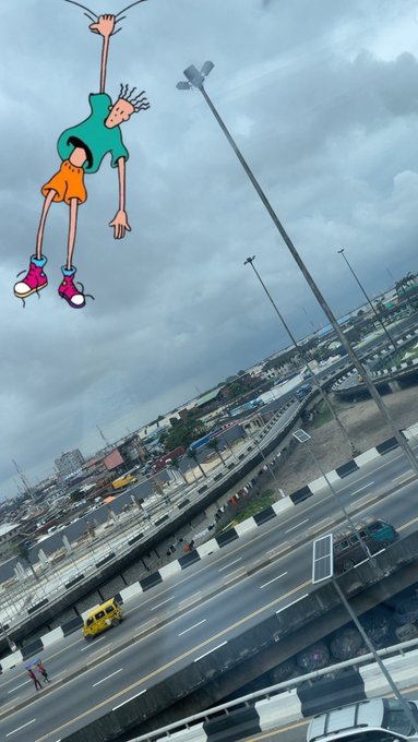 A cartoon character decal on a window shows a person hanging upside down over a view of a highway and cityscape under a cloudy sky.