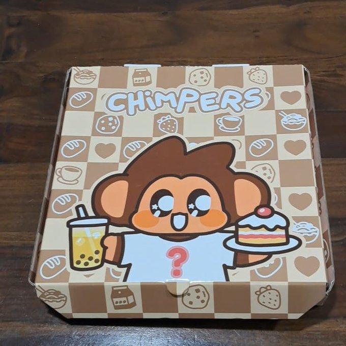 A cardboard box labeled 'CHIMPERS' sits on a wooden surface, decorated with a cartoon monkey holding a boba drink and cake, surrounded by a pattern of food icons.