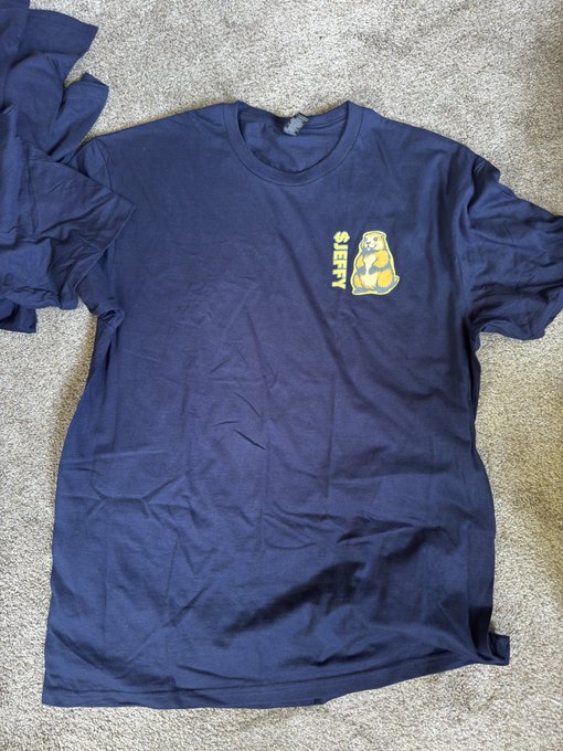Navy blue t-shirt laid on concrete with a small '$JEFF' groundhog graphic on the chest.