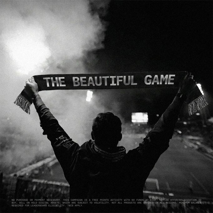 The image features a person holding up a scarf with the words "The Beautiful Game" written on it. The person appears to be at a sports event or stadium, as there are other people visible in the background who seem to be watching the game. The focus of the image is on the individual and their support for the sport, which can be seen through the use of the scarf with the words "The Beautiful Game" written on it.