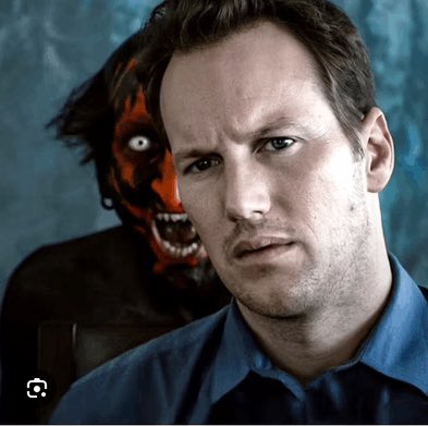 A man in a blue shirt looks seriously at the camera while a demonic red-faced figure with fangs lurks menacingly over his shoulder in the background.