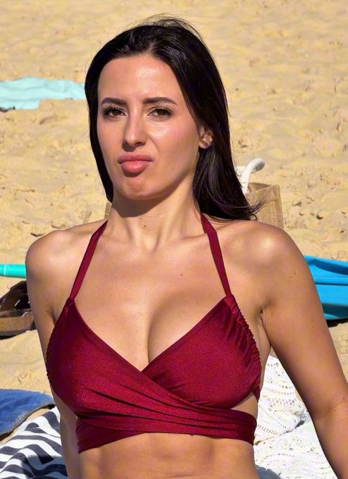 A woman with dark hair wearing a burgundy bikini top, photographed on a sandy beach.