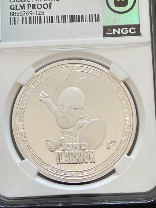 A silver 'GEM PROOF' NGC-graded coin featuring a 'Kind Warrior' cartoon character holding a sword and shield, with a certification number of 8856269-125.