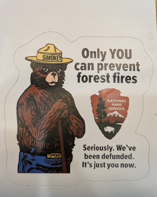 A modified Smokey Bear sticker with text reading 'Only YOU can prevent forest fires. Seriously. We've been defunded. It's just you now.' alongside the National Park Service arrowhead logo.