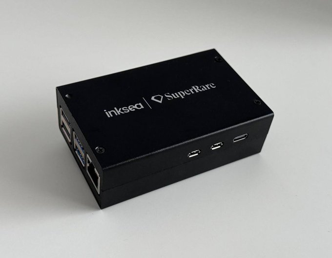 A black rectangular metal case labeled 'inksea' and 'SuperRare' sits on a white surface, displaying various ports including USB and Ethernet.