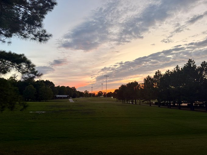 A peaceful sunset illuminates a tranquil park with scattered clouds glowing orange and pink over an open grassy field framed by trees. The serene scene complements the hopeful, restful sentiment of saying goodnight to the Bitcoin community with optimism for the future.