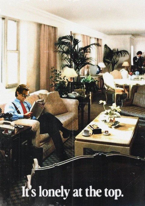 A vintage photograph showing a man in a suit sitting alone reading in a spacious, empty living room, with the caption 'It's lonely at the top.' at the bottom.