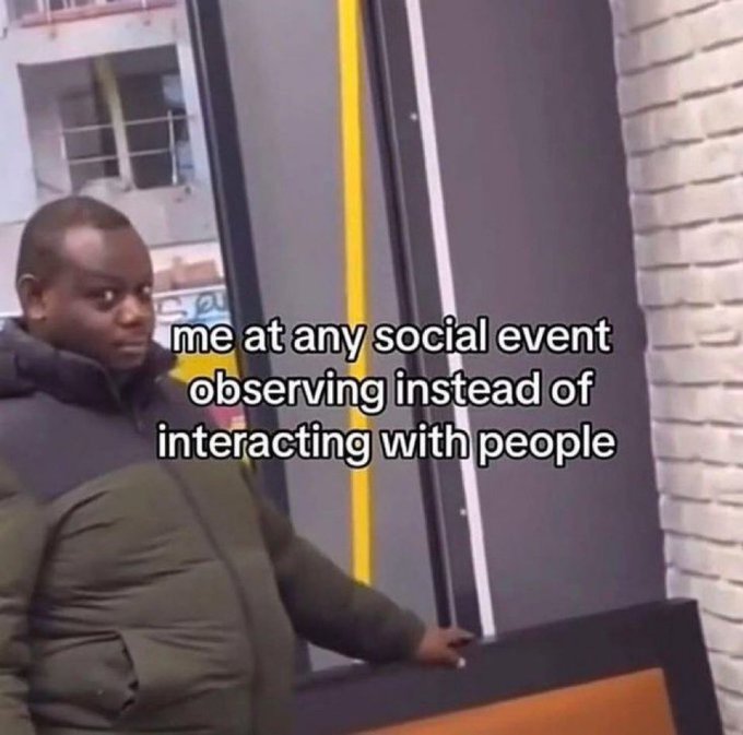 A young person in a puffy green jacket stands against a brick wall, glancing sideways with a reserved expression. The overlaid text reads: "me at any social event observing instead of interacting with people."
