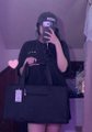 A low-resolution mirror selfie of a person wearing a dark hoodie, cap, and mask, holding a phone to take the picture in a dimly lit setting.