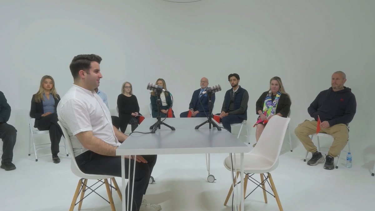 Two crypto experts (one seated at a white table, another on the far right) face off against a panel of ten traditional bankers seated in a semicircle in a minimalist white studio, capturing the "2 vs. 10" crypto vs. banking debate setup for EtherFi.