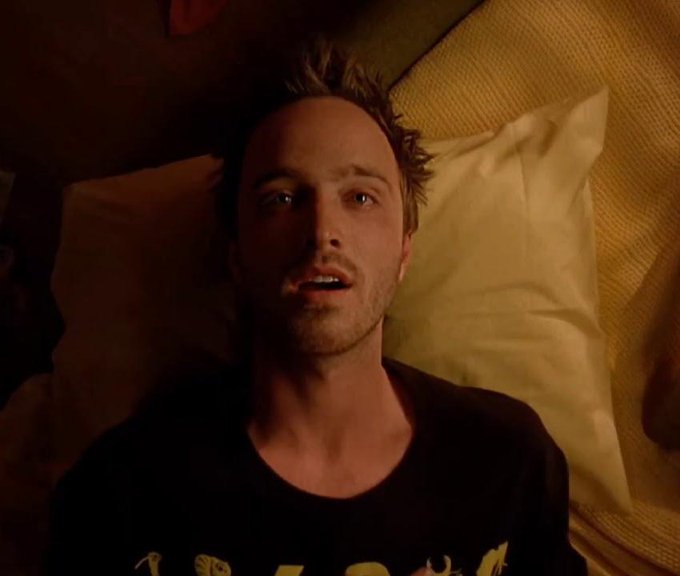 A still of actor Aaron Paul from the TV show 'Breaking Bad,' lying on a bed with a startled, wide-eyed expression.
