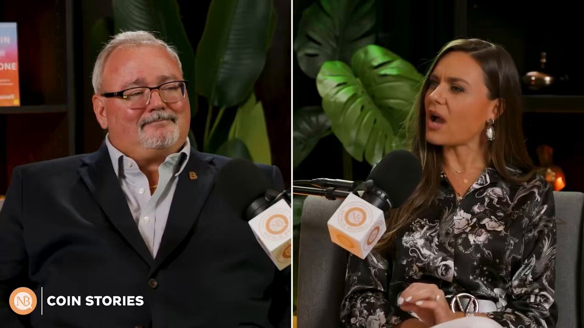 The image features two men sitting next to each other with microphones, appearing to be discussing something related to Bitcoin or cryptocurrency. The man on the left has a beard and glasses, while the man on the right has long hair and is wearing a floral print blouse. They are both seated in chairs, which can be seen in the background of the image.
