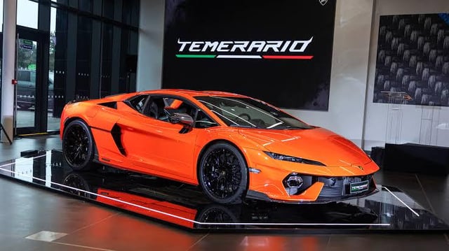 An orange Lamborghini Temerario sports car displayed on a showroom platform with the 'Temerario' name illuminated on the wall behind it.