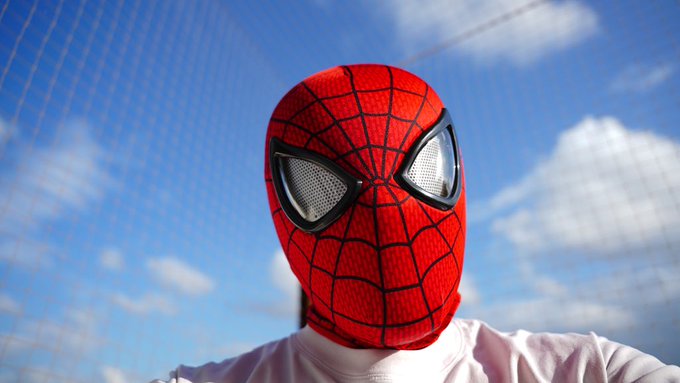 A close-up shot of a person wearing a Spider-Man mask against a blue sky with clouds.