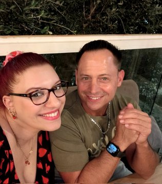 A smiling woman with red hair and glasses sits next to a man wearing a digital watch, both posing together at what appears to be an outdoor dinner in Greece, illustrating the post's joy about finally meeting an NFT community member (@Stone_XRPL) in person after five years in the space.