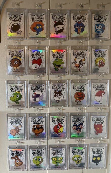 A display of 25 'MEGA HEADS' collectible trading cards in plastic sleeves arranged in a 5x5 grid, featuring various cartoon characters like Super Mario, Hello Kitty, Batman, and a Jack-o'-lantern.