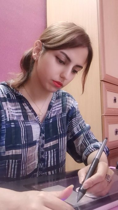 A young woman wearing a plaid shirt is focused on drawing or writing on a digital tablet using a stylus.