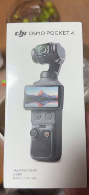 The image shows a person holding the retail box of a DJI Osmo Pocket 4 (Standard Combo), featuring a printed image of the gimbal camera with its articulating screen displaying a mountain landscape. The caption relates to the post by showcasing the DJI Pocket 4 that was received as a KOL gift from Binance.