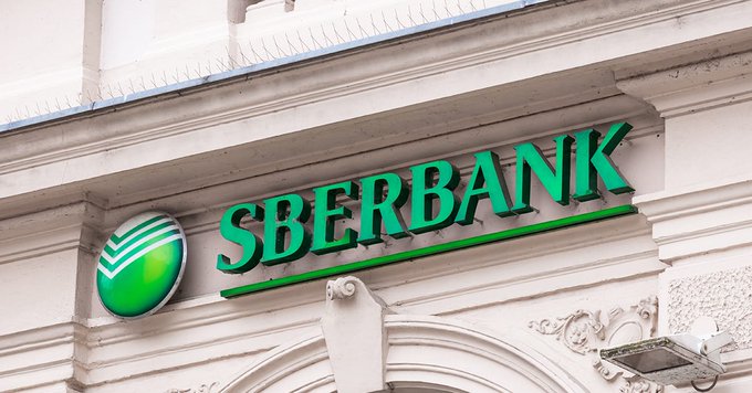 The image shows the green "SBERBANK" logo and emblem mounted on the exterior of a building, representing Russia's largest bank as it prepares to launch new cryptocurrency wallet and digital asset custody services.