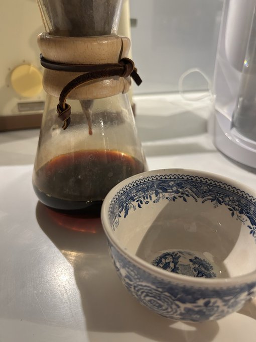 A Chemex coffee maker with dark brewed coffee sits next to an empty blue and white patterned ceramic bowl on a white countertop, capturing a late-night "glue session" prep ritual. The image illustrates the accompanying post about staying up late fueling up on coffee to work on a WSOP x Solana project.