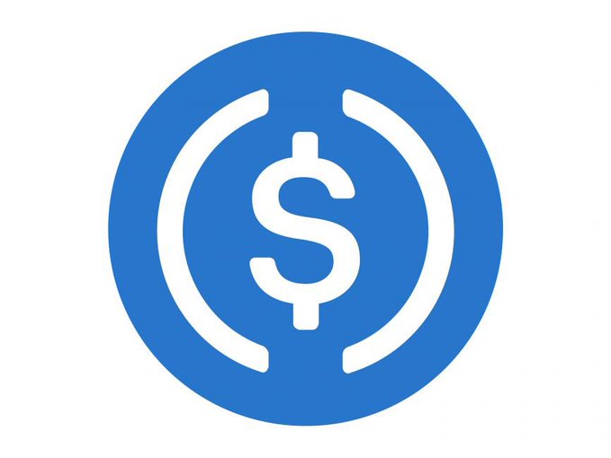 A blue circular logo featuring a white dollar sign symbol flanked by two white curved lines, which appears to be the USDC (USD Coin) cryptocurrency logo.
