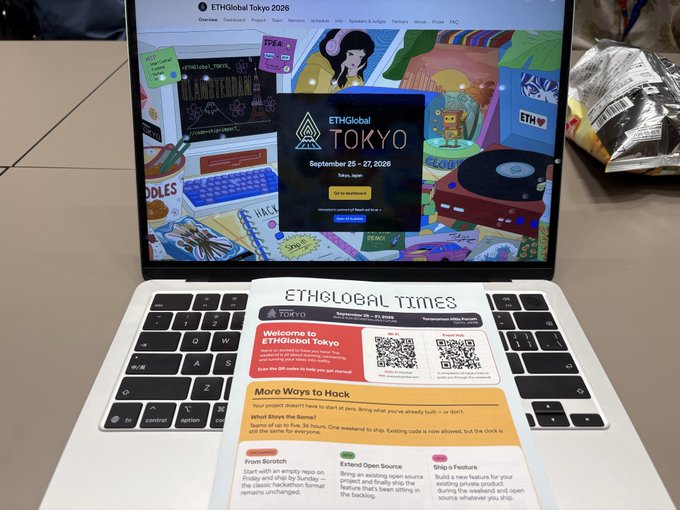 A laptop open to the ETHGlobal Tokyo 2026 event webpage (September 26-27, 2026), with an 'ETHGLOBAL TIMES' welcome flyer placed on the keyboard offering prizes like bounty, feature spots, and extend open source for hackers.