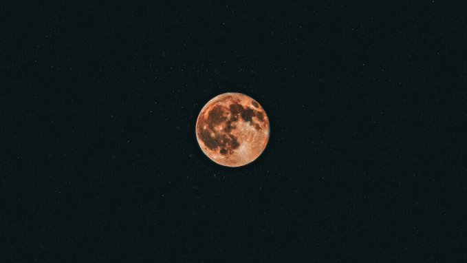 A glowing, reddish-orange full moon is centered against a dark sky speckled with tiny stars.