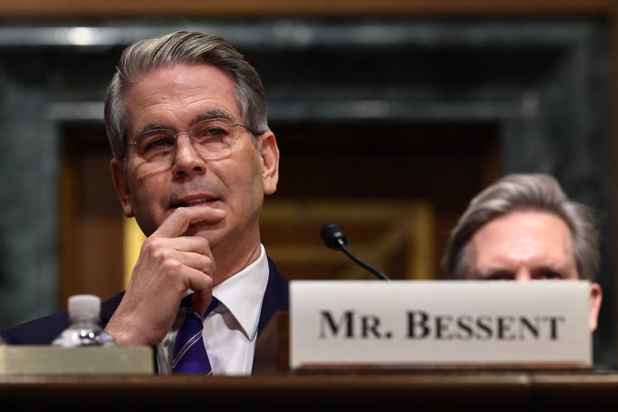 Treasury Secretary Scott Bessent testifies before a Senate panel, with a nameplate reading "MR. BESSENT" visible at the witness table. The image accompanies his remarks advocating for passage of the Clarity Act to establish clear crypto regulations as a national priority.