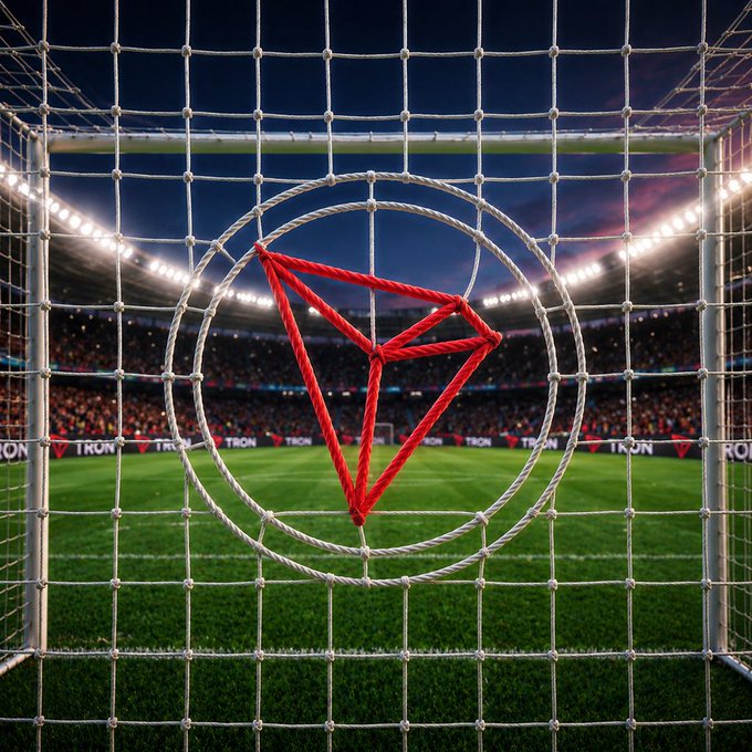 A goal net shaped with the TRON logo (a red triangle inside a white circle) is set against a packed stadium backdrop, symbolizing TRON's unstoppable "scoring" performance in blockchain security. The "TRON" branding on the field reflects how its Delegated Proof of Stake acts as the ultimate defense, blocking threats while advancing the network forward.