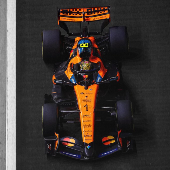 A top-down view shows an orange-and-black McLaren Formula 1 car, number 1, on a dark track, with the “WAGMI views from the top” caption fitting the elevated perspective.