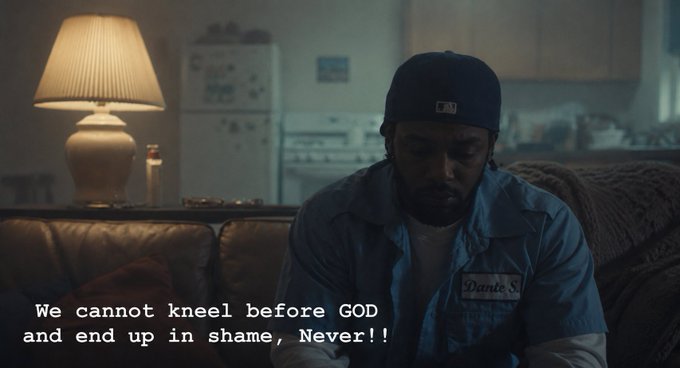 A dimly lit scene of a man wearing a blue shirt and baseball cap sitting on a leather couch, with subtitles reading 'We cannot kneel before GOD and end up in shame, Never!!'