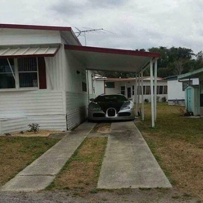 A silver Bugatti Veyron parked under a carport attached to a white mobile home, with a TV antenna visible on the roof.